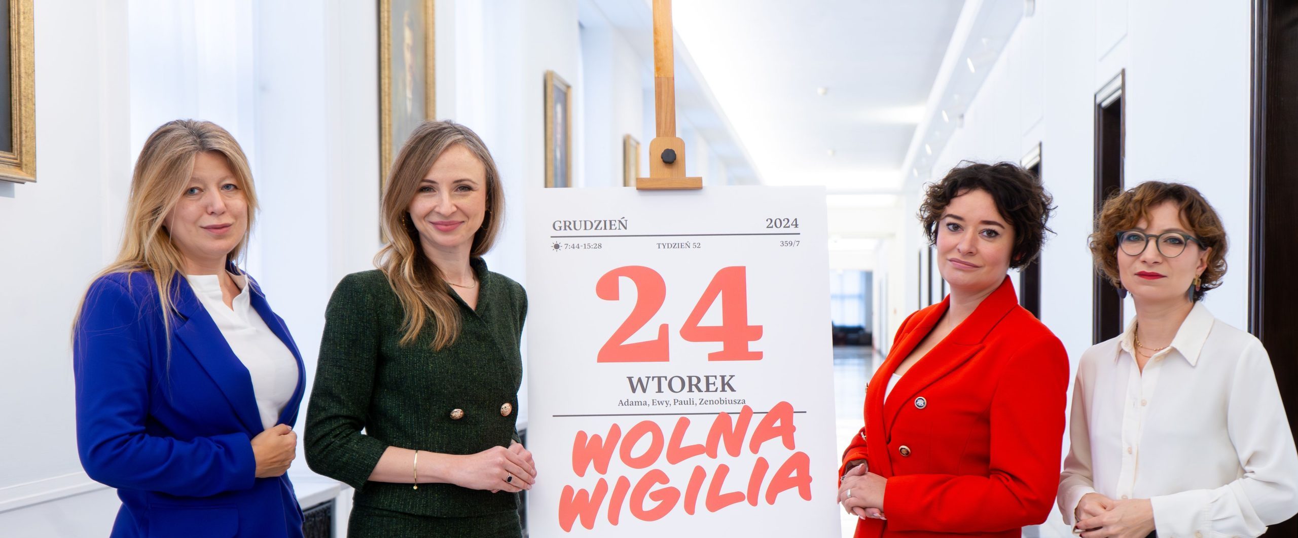 Posłanki Lewicy stoją obok dużego kartki kalendarza z napisem „24 grudzień Wtorek Wolna Wigilia” w jasnym korytarzu.
