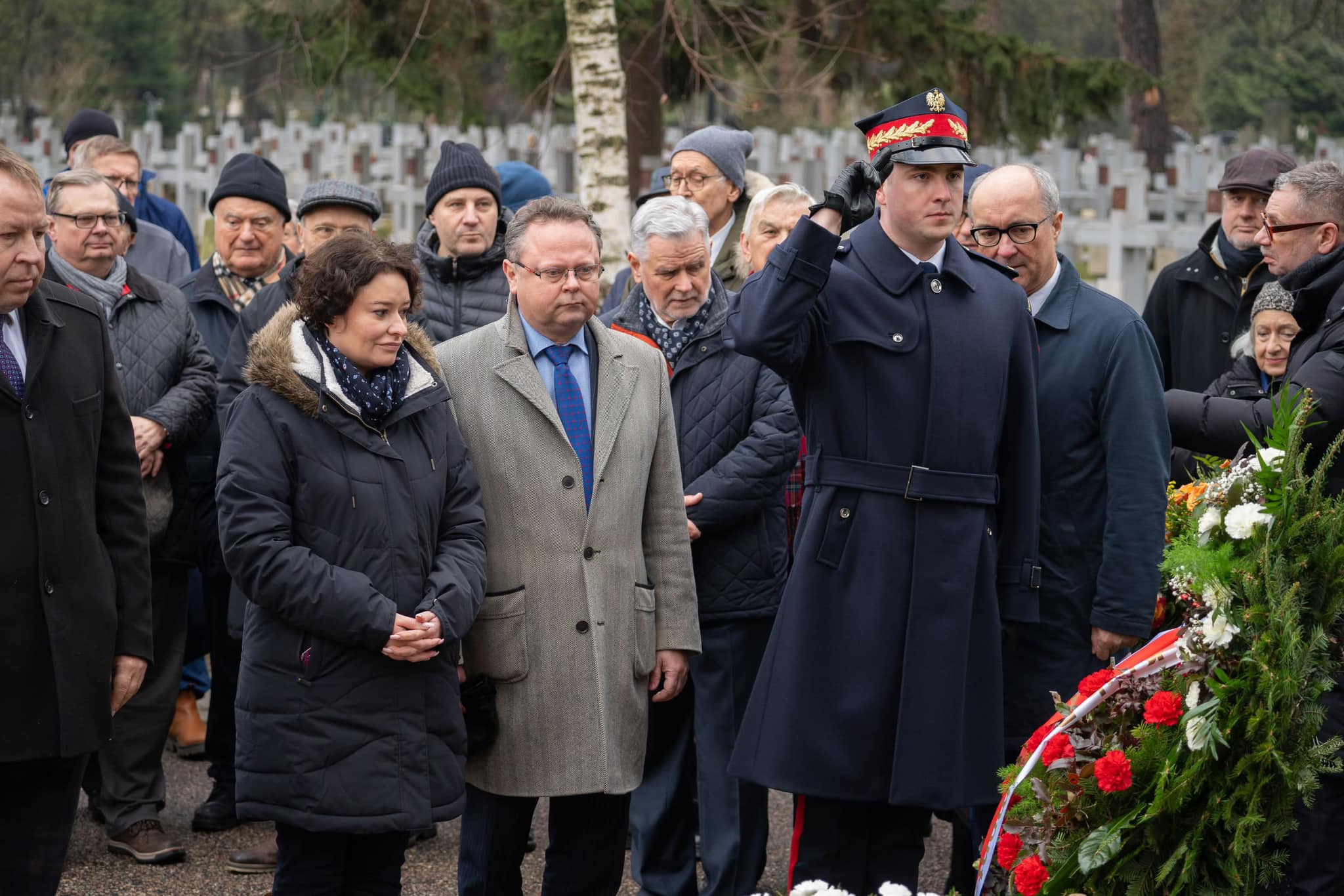 Grupa osób składająca hołd przy grobie Józefa Oleksego na cmentarzu, wśród nich żołnierz oddający salut.