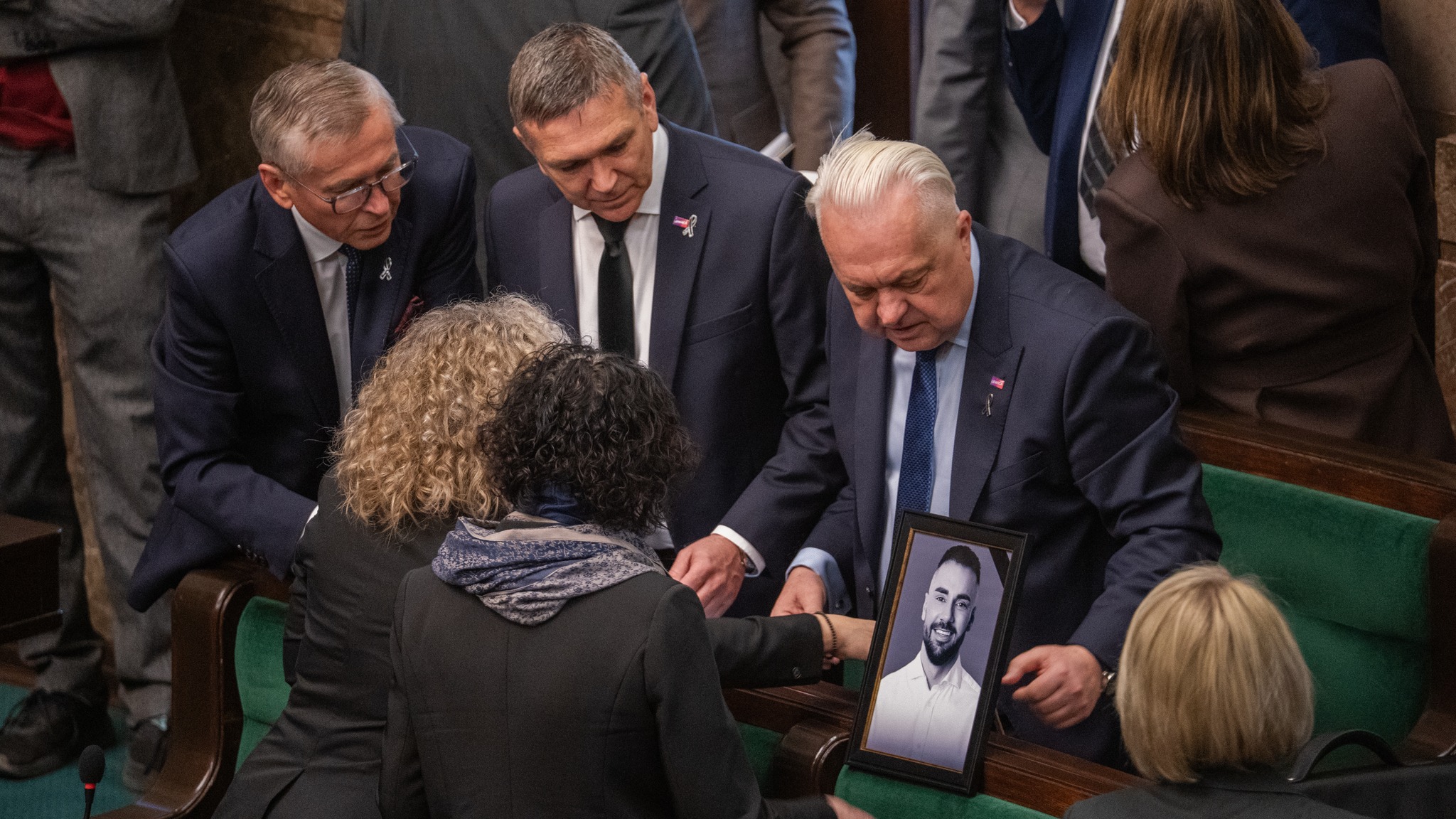 Politycy w żałobnych strojach składają kondolencje rodzinie zmarłego, trzymając jego portret.