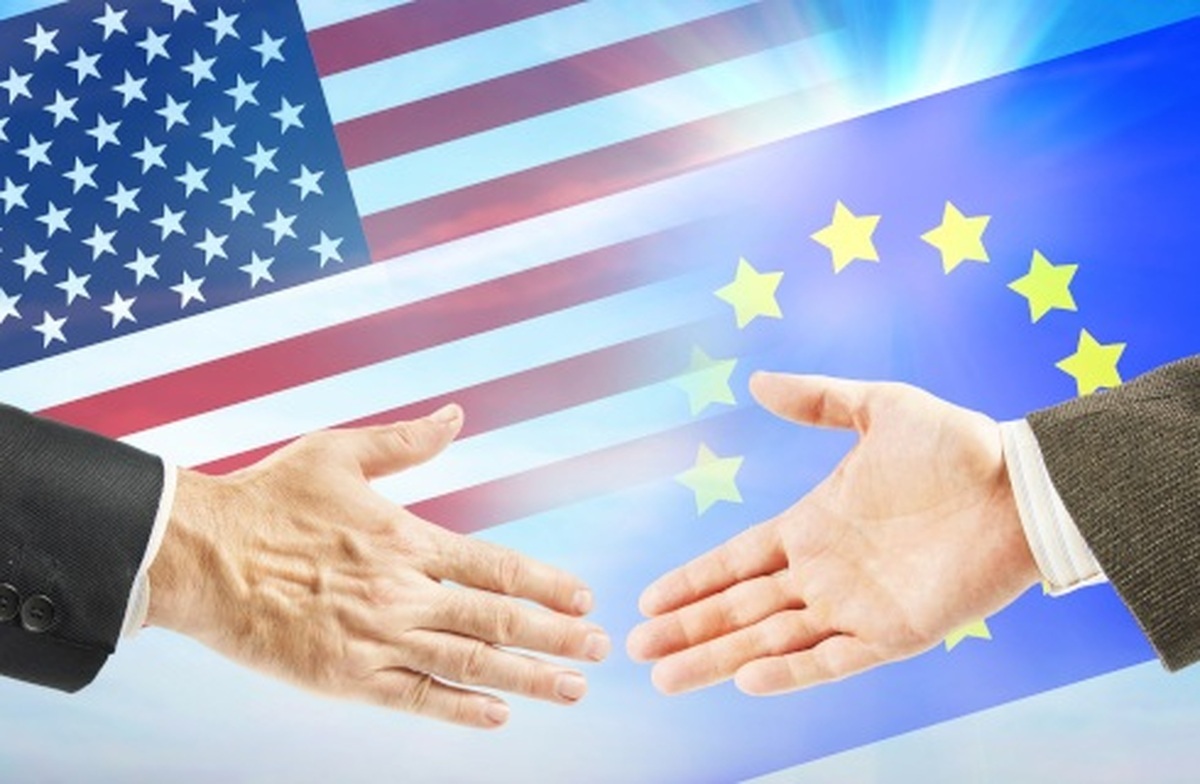 Dwie wyciągnięte dłonie na tle flag USA i Unii Europejskiej symbolizujące współpracę i wsparcie w ramach NATO.