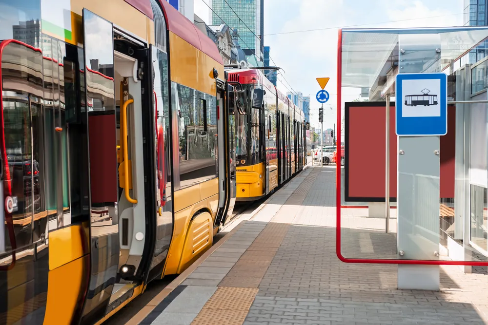 Nowoczesny żółto-czerwony tramwaj stoi na przystanku w miejskim otoczeniu.